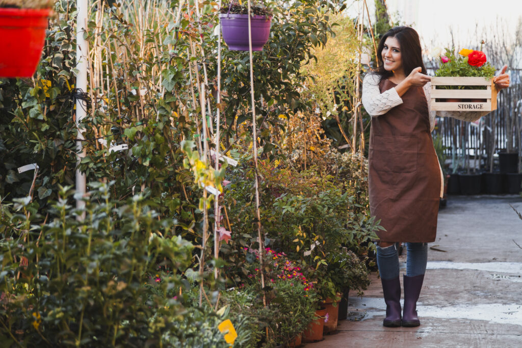 settling-new-garden-spring-planting Woman holding a crate of flowers in a garden nursery, preparing for spring planting in a new home.